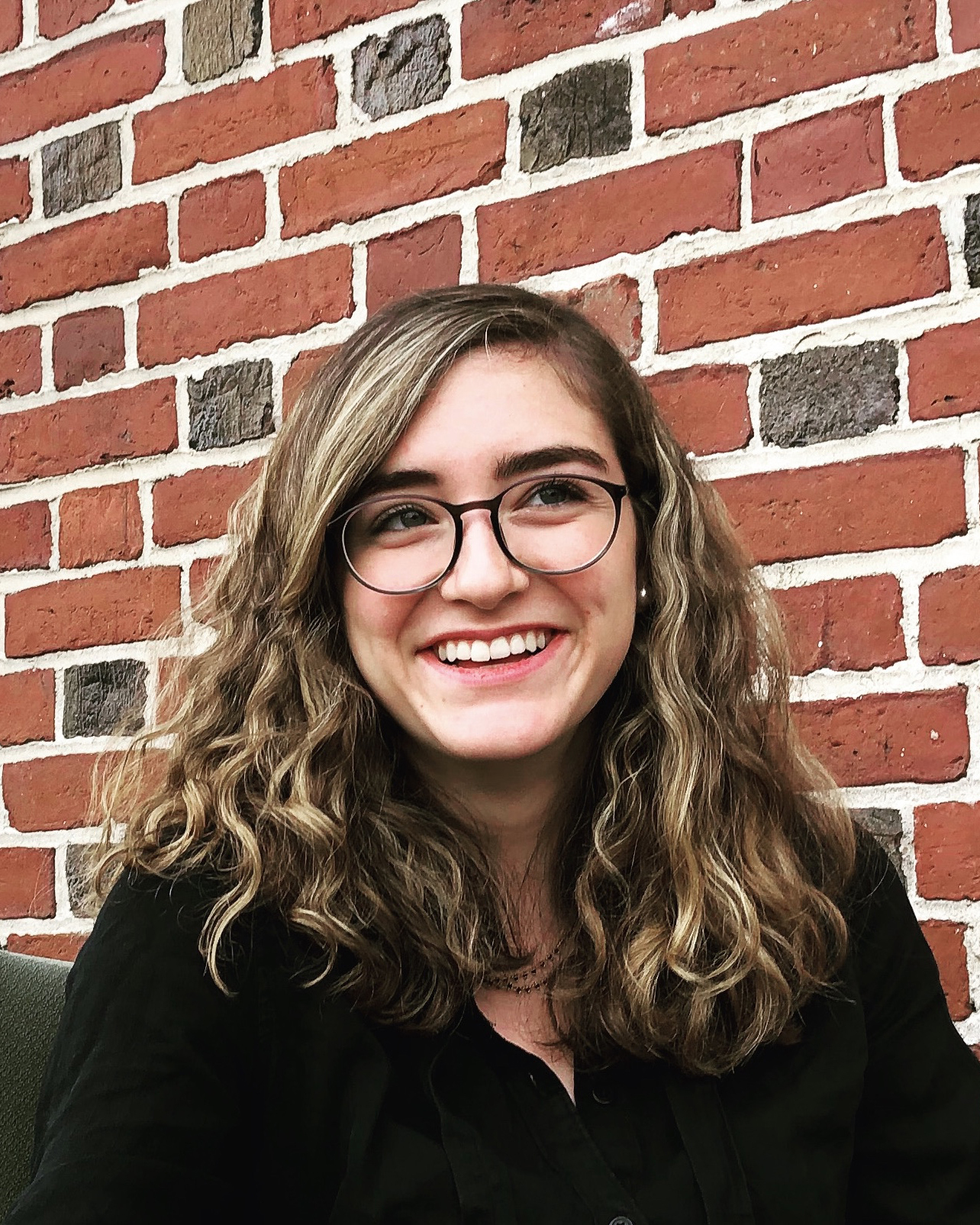 Caroline Cook, the Summer 2018 Historical Accountability Student Research Fellow,  photographed in front of a  red brick wall.