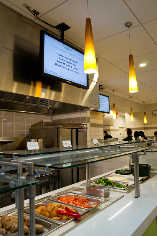 College kitchen serving vegetables and with TV screen above 