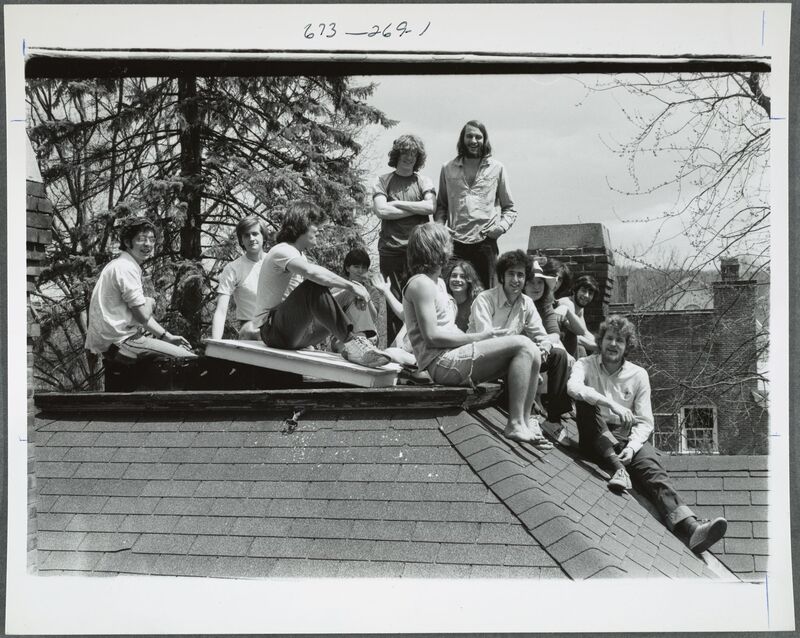 Image of a dozen students (men and women) sitting and standing on a roof in the sunlight