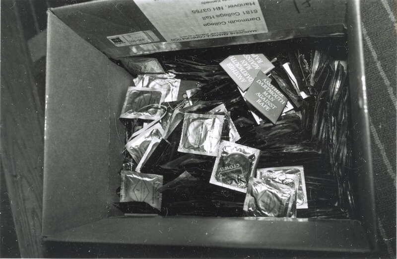 A cardboard box full of wrapped condoms and a few badges that read, "Another Dartmouth Man Against Rape."
