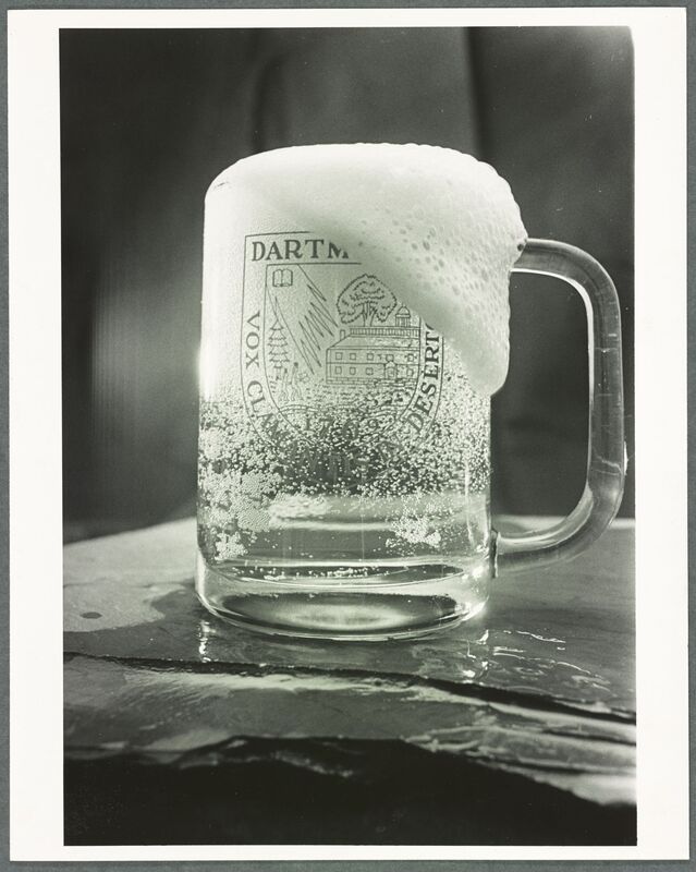 Black and white photograph of a singular overflowing beer glass, engraved with the Dartmouth seal.