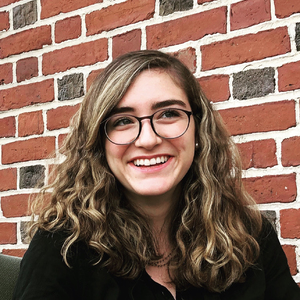 Caroline Cook, the Summer 2018 Historical Accountability Student Research Fellow,  photographed in front of a  red brick wall.